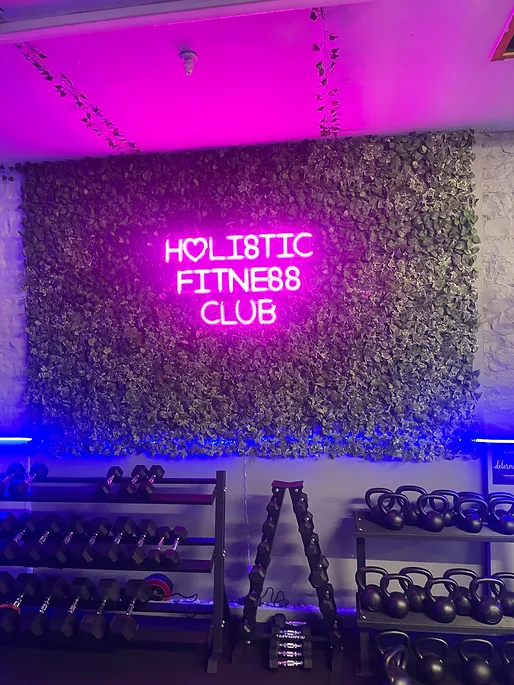 an image of a wall in Holistic Fitness Club with a neon sign of the club's name above various weights